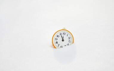 Yellow alarm clock in the snow. Winter coming concept.