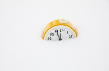 Yellow alarm clock in the snow. Winter coming concept.