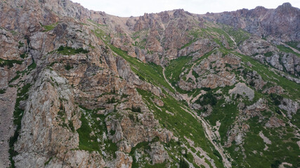 Drone view of a green gorge with high rocky cliffs. A grey, bubbling river is running. The sky was overcast. Lots of big rocks and coniferous trees. Wildlife of Kazakhstan. Gorges of Burkhan Bulak