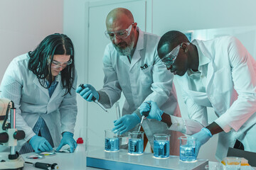 Three Scientists Working with Beakers in the Lab - A diverse team of researchers engages with beakers on a hot plate, captivated by the effervescing blue solution. - obrazy, fototapety, plakaty