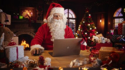 Merry Santa Claus Sitting Behind a Desk and Working on Laptop Computer. Senior Santa Shopping Online, Fulfilling Gift Orders for Christmas and New Year. Advertising Footage for Winter Holidays