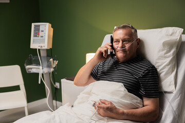 Elderly man, with an oxygen tube for breathing assistance, talks on the phone as he receives treatment