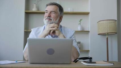 Older man working online with laptop computer at home sitting at desk. Home office, surfing internet