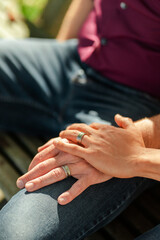 Portrait of homosexual couple sitting on bench holding hands, selective focus on rings, closeup
