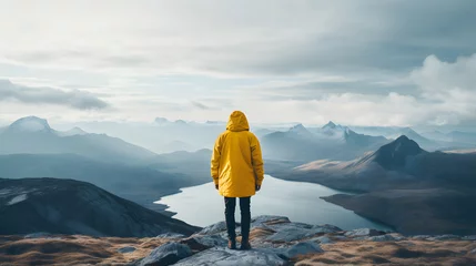 Poster Man in yellow raincoat standing on top of mountain and looking at lake © Andsx