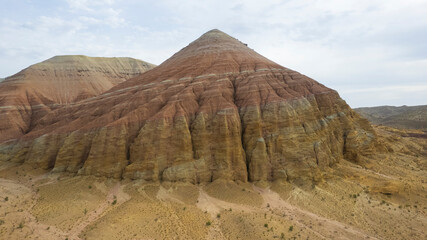 Colorful high mountains and a canyon made of clay. A large gorge with different rocks and different colors. Red, orange, white and yellow flowers of the walls of the rocks. A tourist walks. Aktau