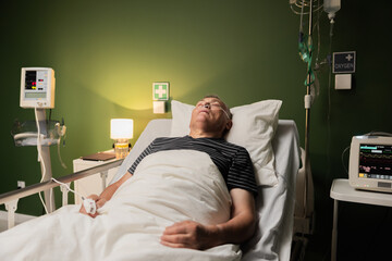 Elderly man in a hospital room, using an oxygen tube for respiratory support, within a ward