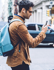 Hispanic young man walking down street and messaging on cellphone