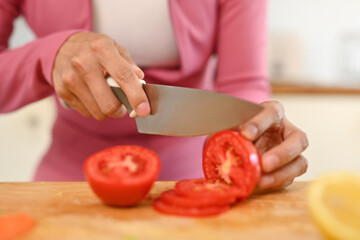 Woman cutting tomato with knife, preparing healthy breakfast in kitchen. Healthy food concept