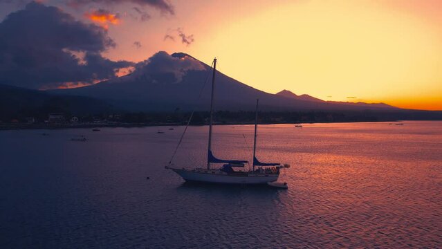 Sunset at Amed with yacht anchored in shallow sea and mount Agung in background in Bali, Indonesia. Aerial Drone view 4K.