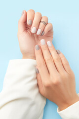 Obraz na płótnie Canvas Womans hands with gray nail design on blue background