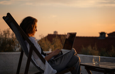 Young woman works on laptop on terrace above old town and sea