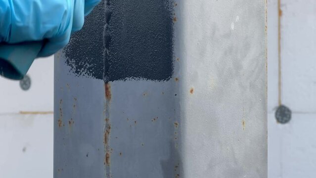 A left-hander in a blue glove paints metal columns with a roller. Concept of repair and construction. Materials and tools for construction. Special anti-corrosion paint for iron.