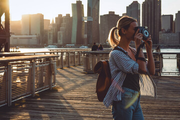 Young female tourist with rucksack taking pictures of evening city - obrazy, fototapety, plakaty
