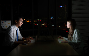 Both of young Asian broker international stock traders working together on desktop at night office, International financial investment company concept