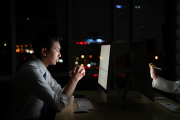 Young Asian broker international stock traders working at night in office using computer and...