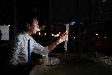 Young Asian broker international stock traders working at night in office using computer and thinking.