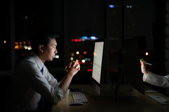 Young Asian broker international stock traders working at night in office using computer and thinking.