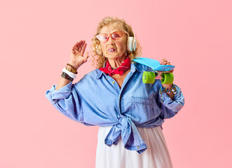 Hipster vibe. Senior beautiful woman in stylish casual clothes, shirt, skirt and sunglasses posing with skateboard over pink background. Concept of emotions, fashion, elderly people, lifestyle. Ad