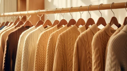 Schilderijen op glas a collection of light brown sweaters neatly arranged on hangers in a well-lit and stylish boutique setting. the classic and timeless appeal of these sweaters. © lililia