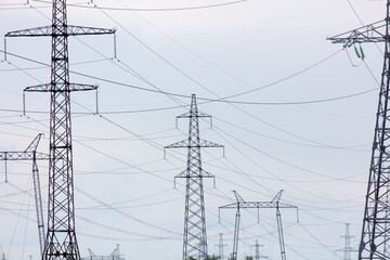 Metal electric poles against a gray sky with clouds