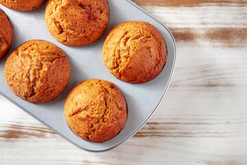 Orange muffins in a muffin tin on a rustic wooden kitchen table, easy baking, overhead flat lay shot with copy space