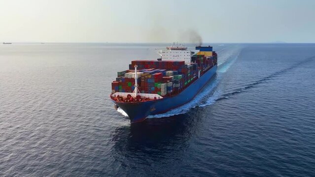 Aerial view of a large container cargo ship traveling with speed over calm ocean and sunset light