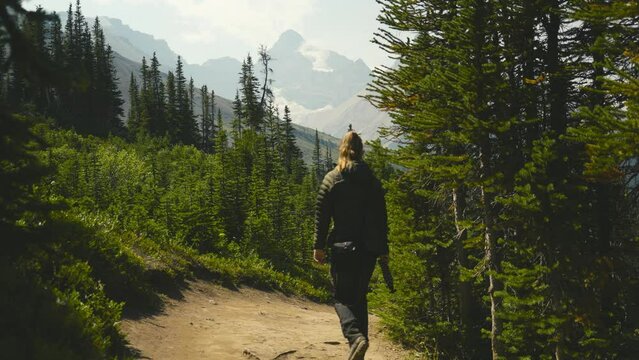 A cinematic shot of a women hiking in the woods of Alberta, on the Parker Ridge hike in Canada, over looking mountains and the stunning scenery of the Rocky Mountains