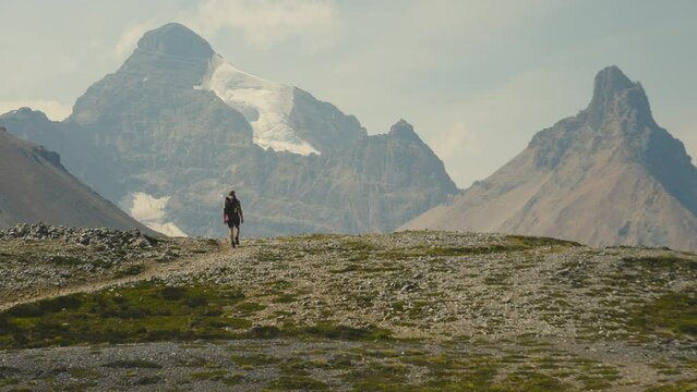 A cinematic clip of a man hiking alone on a mountain peak of Alberta, on the Parker Ridge hike in Canada, over looking mountains and the stunning scenery of the Rocky Mountains