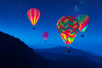 Fototapeta na wymiar Vibrant, glowing hot air balloons against dark night sky rising over mountains.