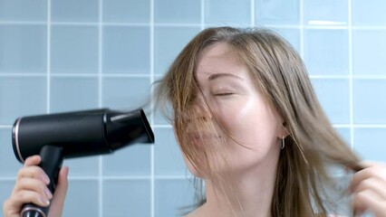 Young woman drying her hair with hairdryer in the bathroom close-up, front view.