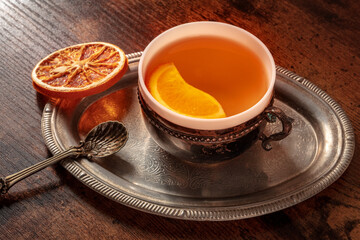 Orange tea with fresh and dried oranges on a vintage tray, a cup on a dark rustic wooden background