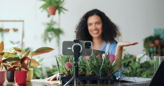 African American woman florist in apron shooting video in flower store using phone. Gardener blogger using phone broadcasting live on smartphone for online shopping in social networks.