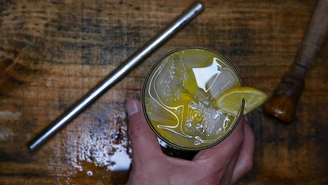 Person holding and shaking a caipirinha with one hand. Person grabbing a Cacha&ccedil;a caipirinha on the table. A beautiful lemon caipirinha on a wet wooden table. Brazilian caipirinha drink recipe.