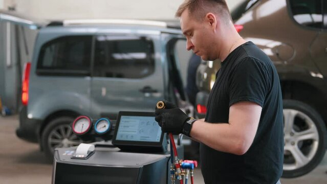 Car mechanic with manometer to fill the gas in the car air conditioning compressor. Service of checking the car air conditioner. Refrigerant recharge system.