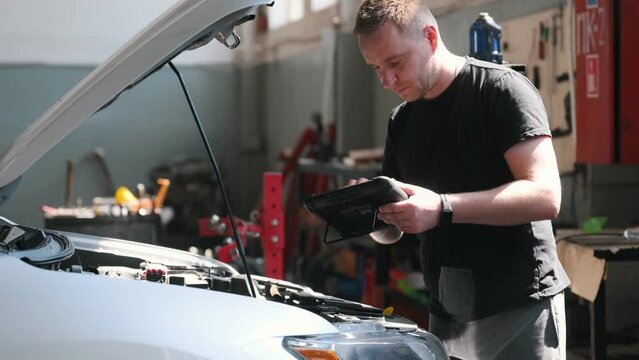 Professional car mechanic working in auto repair service with tablet. Computer diagnostics in garage.