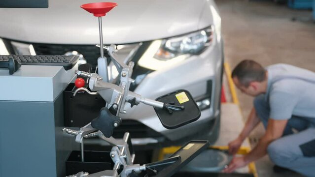 A car service employee installs a wheel adapter with a target on the wheel to perform a wheel alignment. Diagnostics and balancing.
