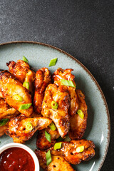 Chicken wings in bbq sauce on craft plate. Top view, close up on black stone table.