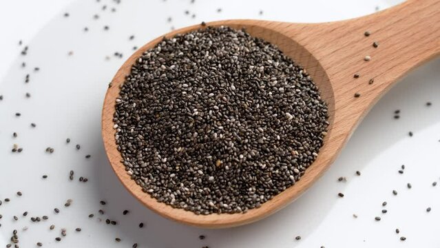 Healthy raw chia seeds in a wooden spoon on white ceramic dish close up. Rotation