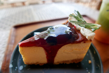 Blueberry cheesecake on a black plate topped with red sauce and decorated with white cream.