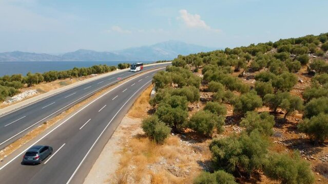 Road trips during holiday season. Cars drive along asphalt mountain road along clean river, sea, ocean and green summer forest. Aerial view from drone. Traveling by road. Bafa Lake