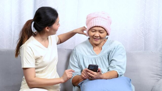 Young Asian daughter spend time with mother cancer patient after chemotherapy survive treatment period, female teaching mom to use modern technology mobile phone shopping online health care knowledge