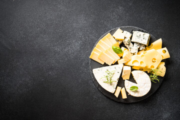 Cheese platter with craft cheese assortment on slate board at black background. Top view with copy...