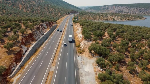 Aerial shot of heavy truck truck by cargo trailer moving through mountains on modern highway along lake or sea. Logistics Delivery Concept. car moving along highway view from drone.