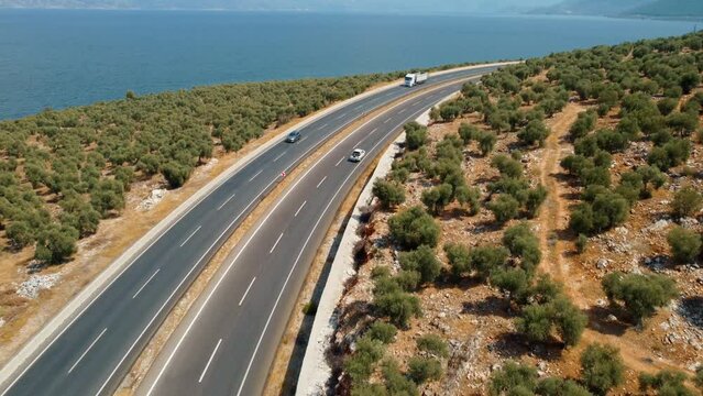Road trips during holiday season. Cars drive along asphalt mountain road along clean river, sea, ocean and green summer forest. Aerial view from drone. Traveling by road. Bafa Lake