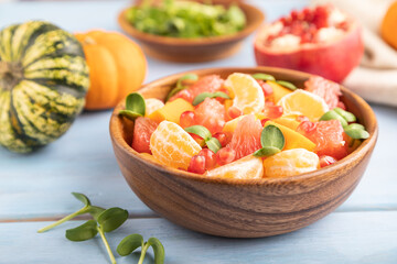 Vegetarian fruit salad of pumpkin, tangerine, pomegranate, microgreen sprouts on blue, side view, selective focus.