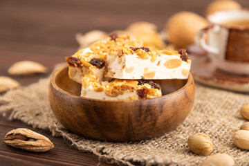 Traditional candy nougat with nuts and sesame on brown wooden, side view, selective focus.