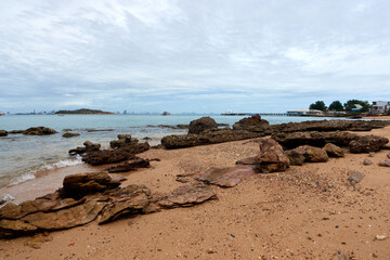 Landscape of rocky beach and sea with distant mountains and islands, blue sky.