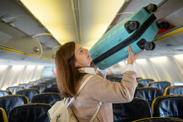 Woman lifting luggage into baggage compartment of airplane cabin