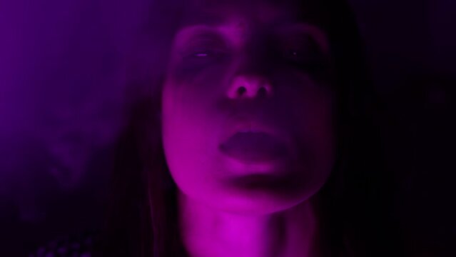 woman drug addict in neon light exhales smoke.